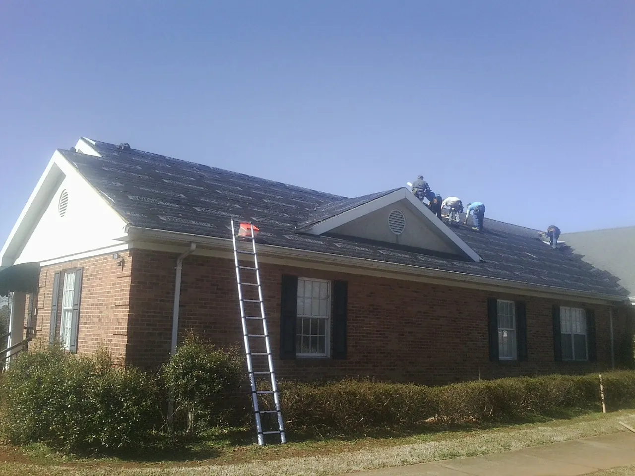 Crew tearing shingles off a brick ranch roof with a ladder set — Metal Roof Repair work by our crew in Leicester