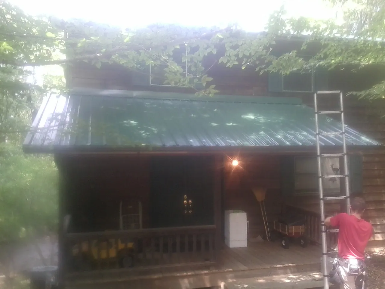 Worker on a ladder at the green porch roof of a wooded cabin in Leicester