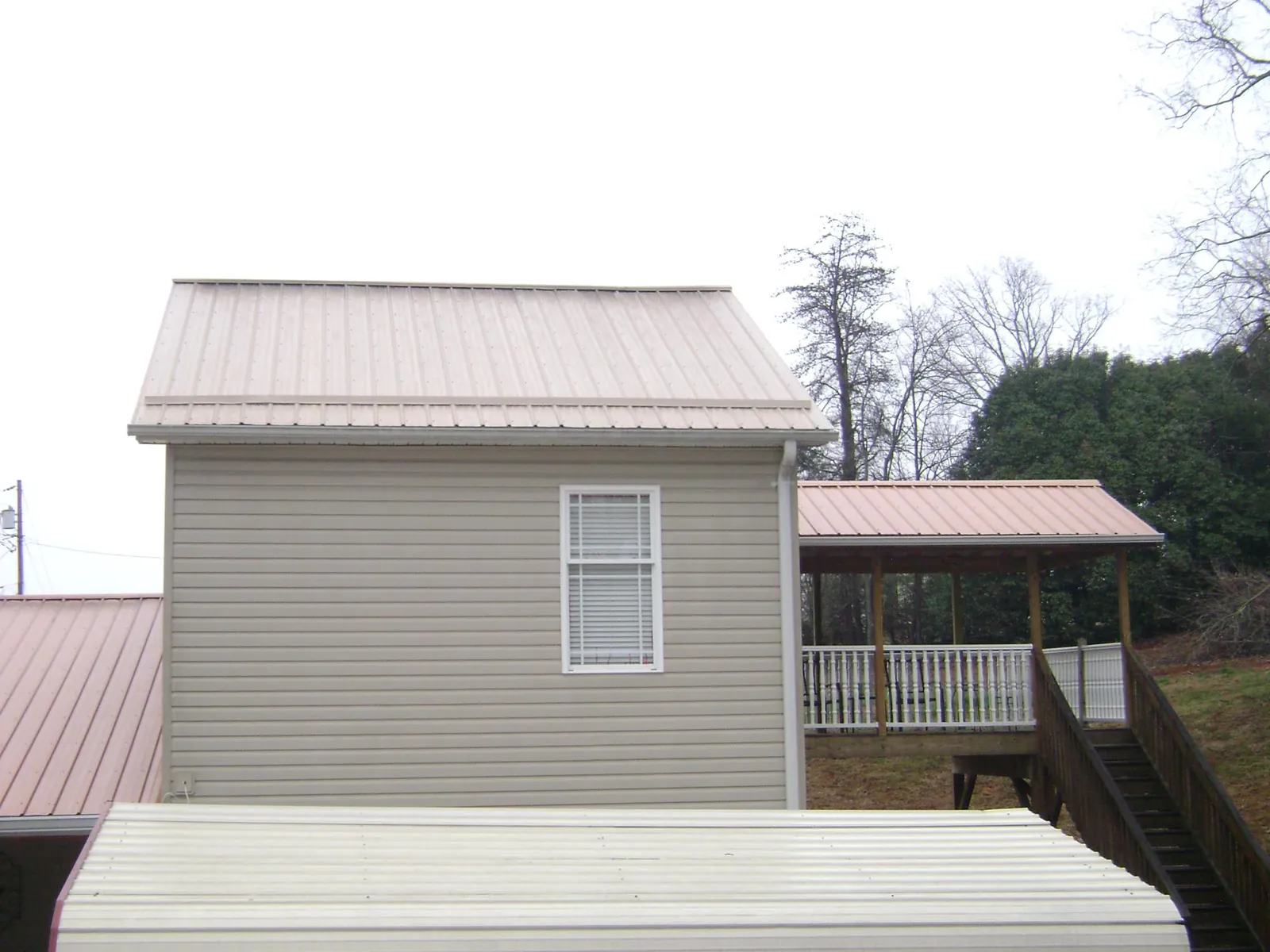 Tan metal roofs on a two story addition and attached porch, from a Roof Replacement job in Leicester